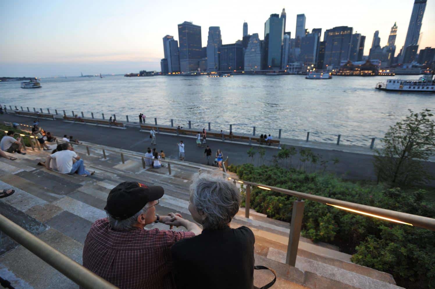 Couple sitting on granite steps overlooking the promenade and East River at sunset.