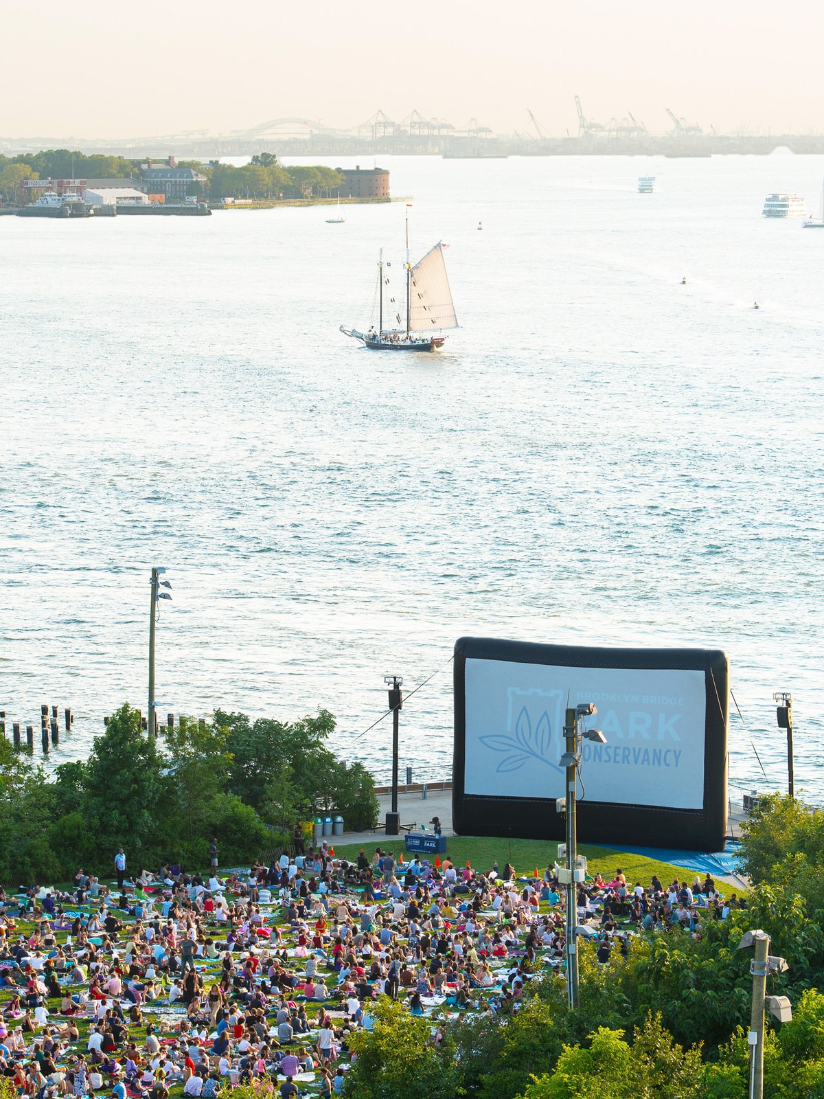 Aerial view of crowd sitting on the lawn facing a large inflatable movie screen at sunset.