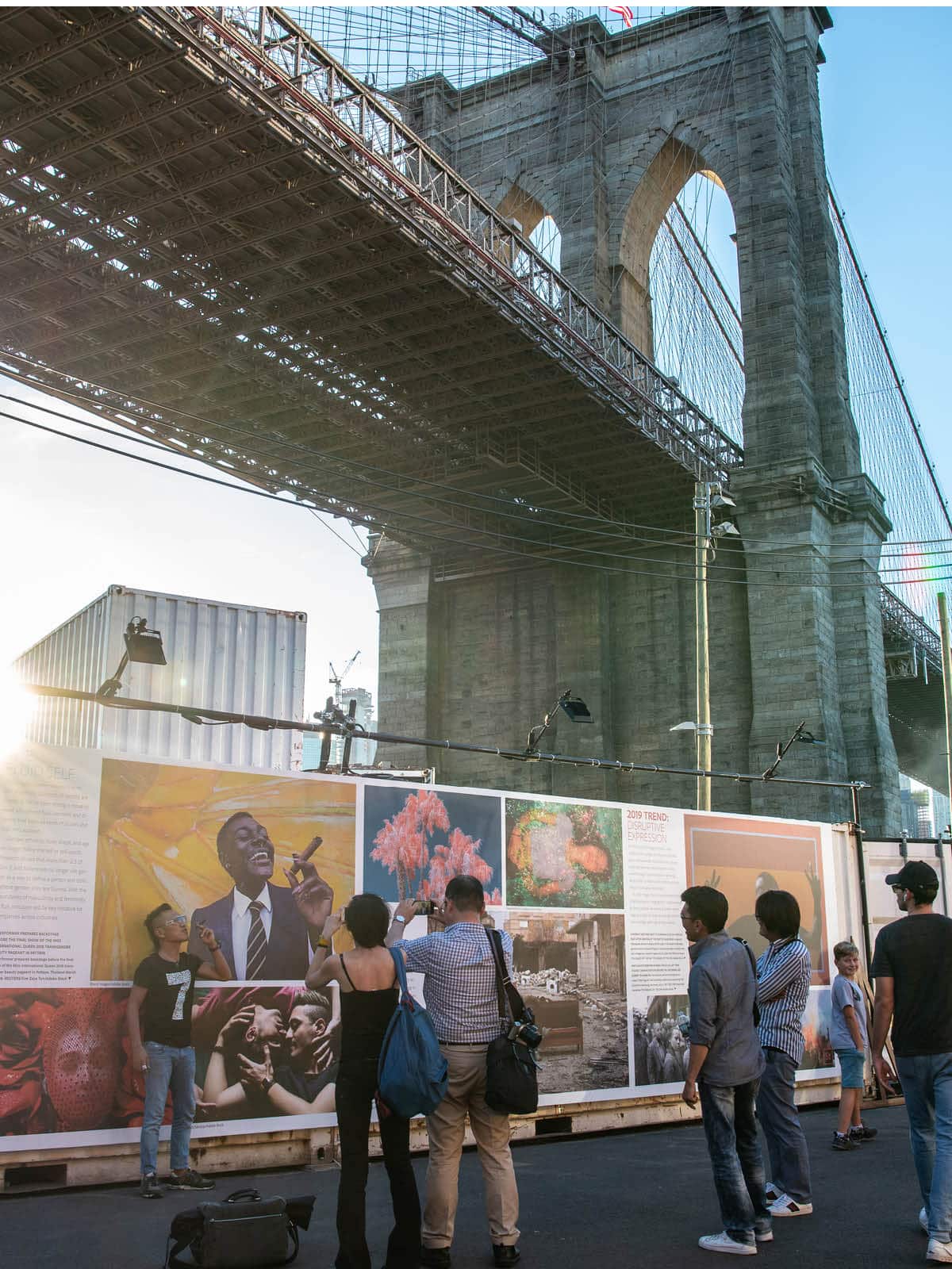 People taking photos of photography display wall under the Brooklyn Bridge, part of Photoville exhibition.