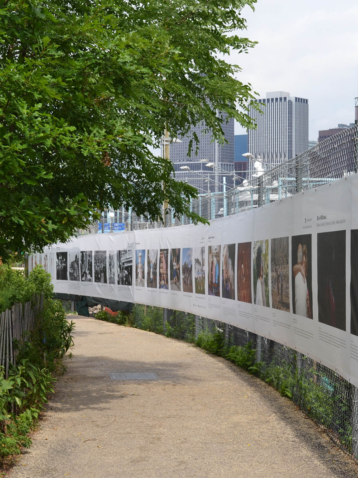 A long photo banner pinned to a chainlink fence along a pathway as part of THE FENCE.